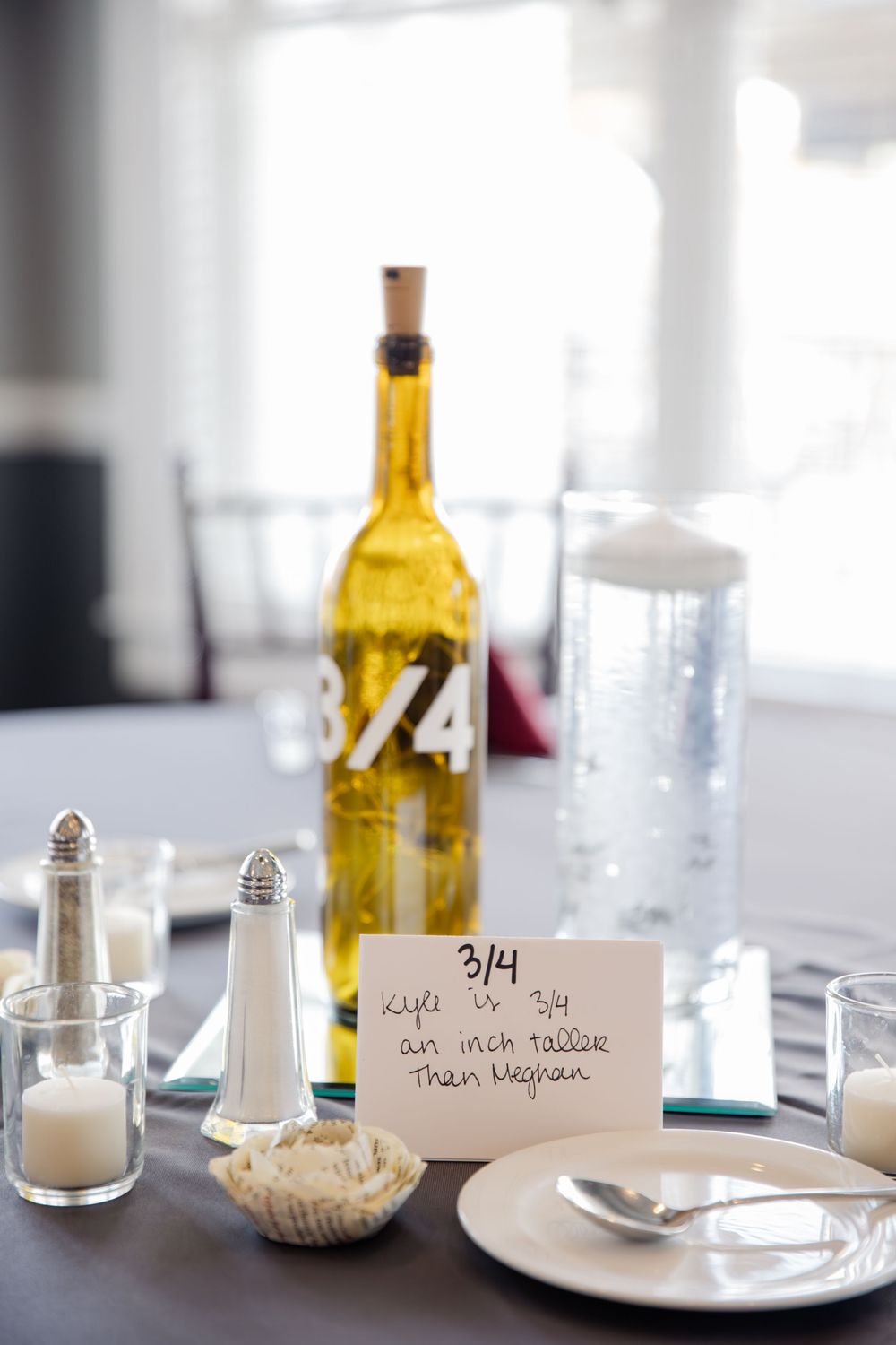 White table settings with wine bottles, salt shakers, and name cards in a bright restaurant interior.