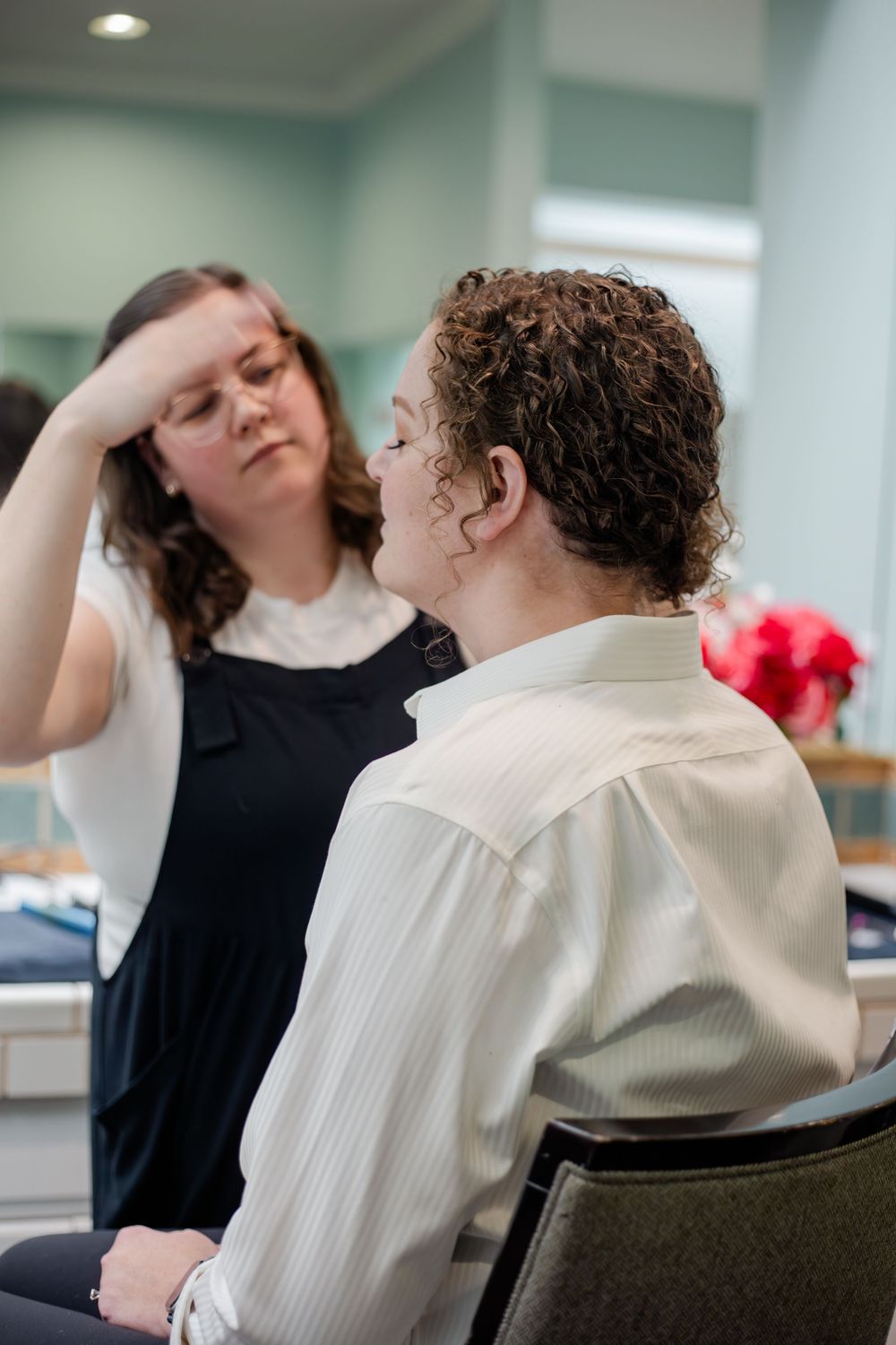 Two people in a medical or therapeutic setting demonstrate physical exercises for neck and shoulder mobility.