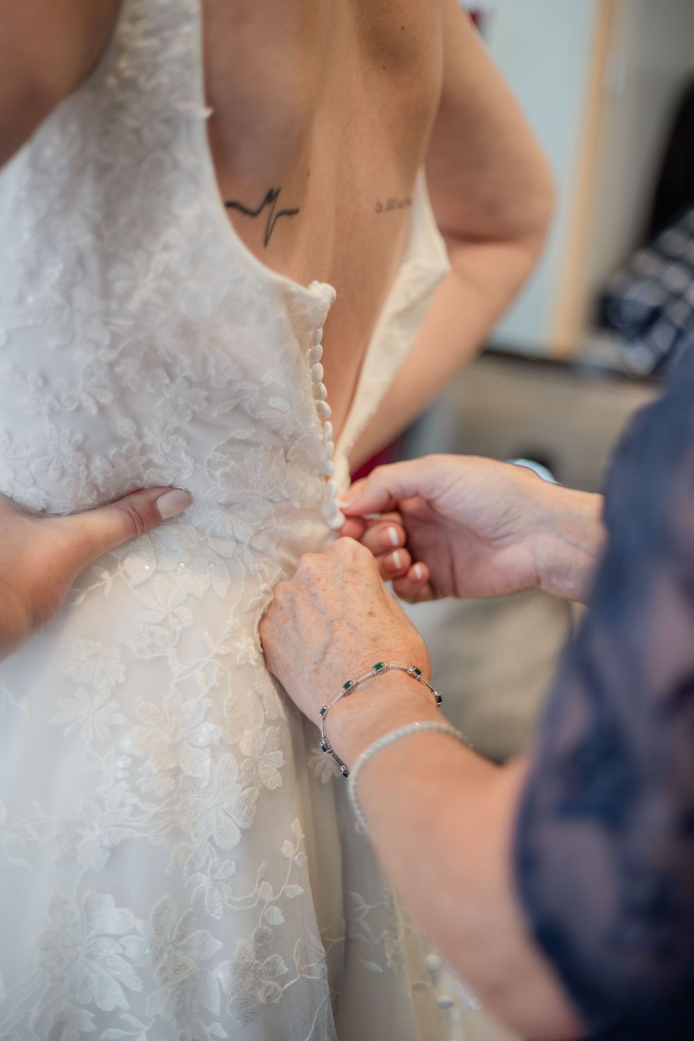 Close-up view of someone helping to lace up an intricate white lace wedding dress.