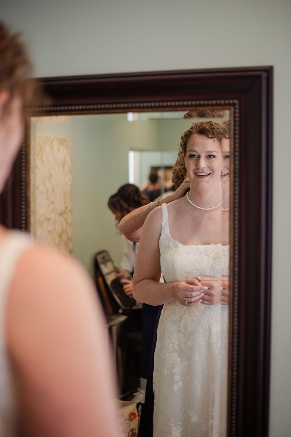 A series of mirror reflections show someone wearing a white dress in a softly lit room with wooden frames.