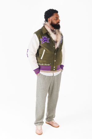 Model wearing olive puffer vest with checkered pants and beige shoes against white background.