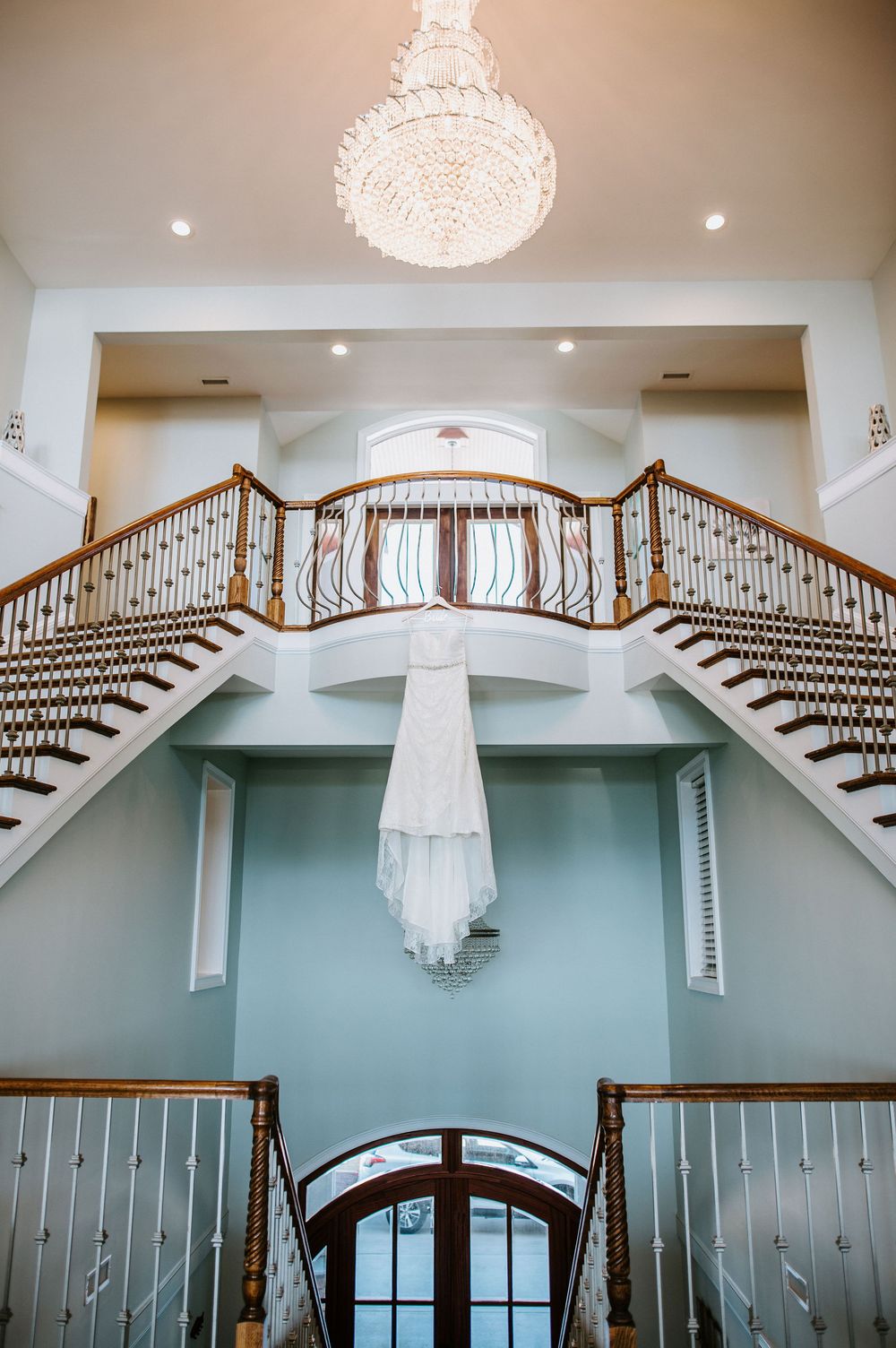 Elegant curved double staircase with wooden railings and crystal chandelier in a grand foyer with mint green walls.