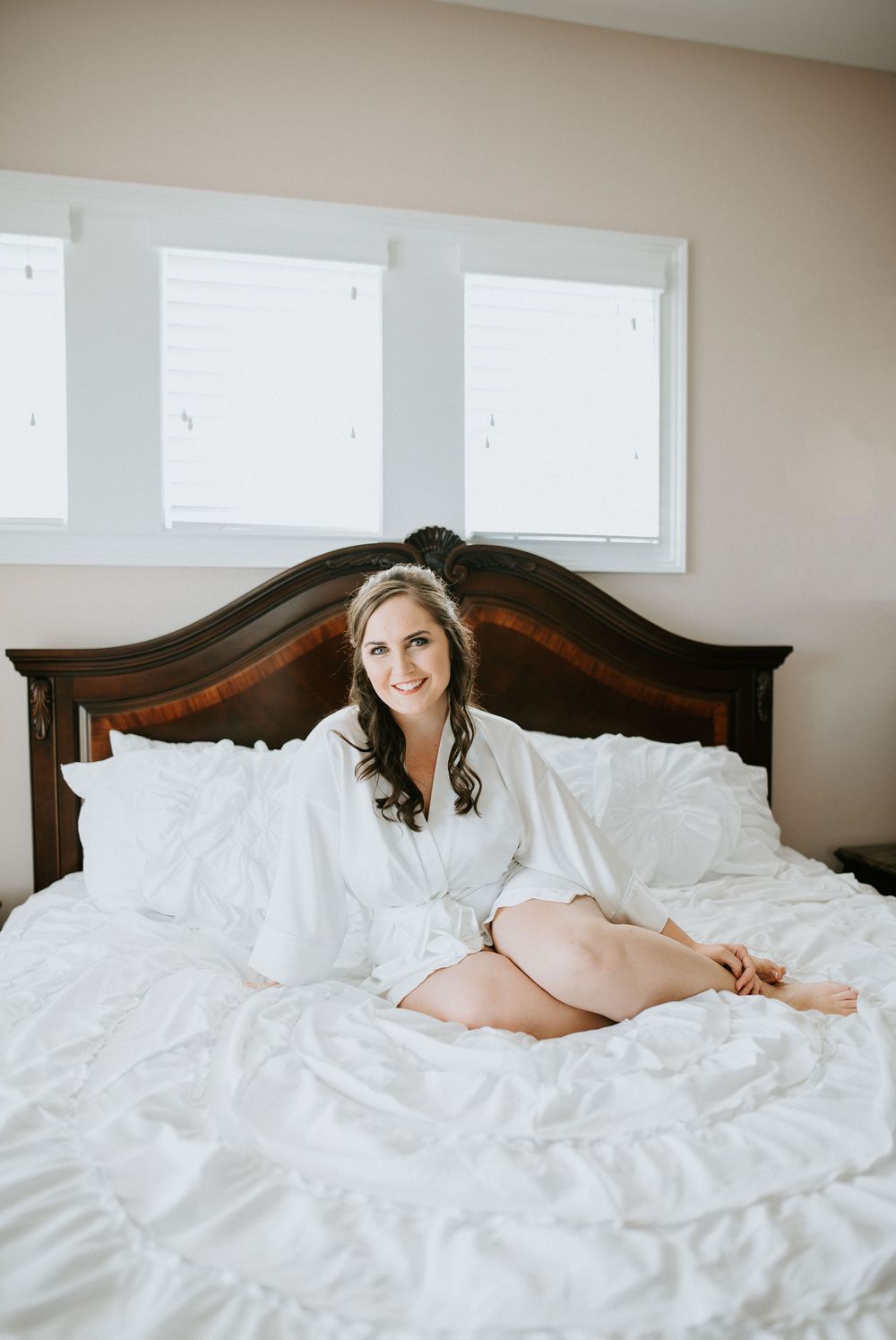 A person in a white robe relaxes on a large bed with white linens against a dark wooden headboard.