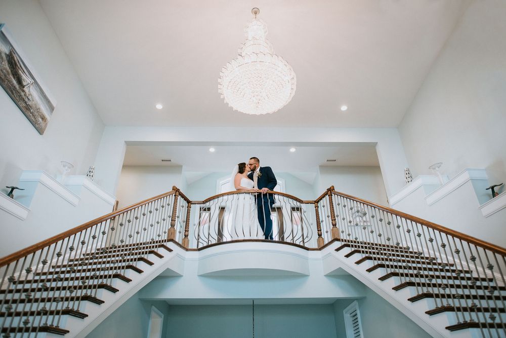 Elegant grand staircase with crystal chandelier in white wedding venue interior.