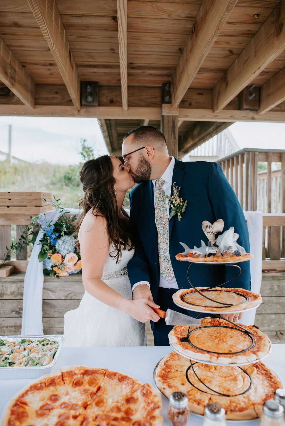 Wedding reception setup with pizza and desserts displayed on rustic wooden tables.