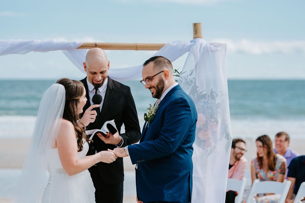 Wedding ceremony on a beach deck with guests watching the couple exchange vows by the ocean.