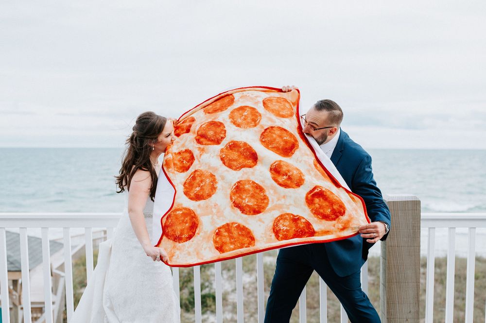 Wedding couple sharing intimate moments by coastal railing with pizza-themed decorations.