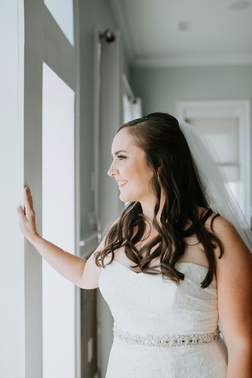 A bride in a flowing white gown and veil poses gracefully against white walls with arched windows.