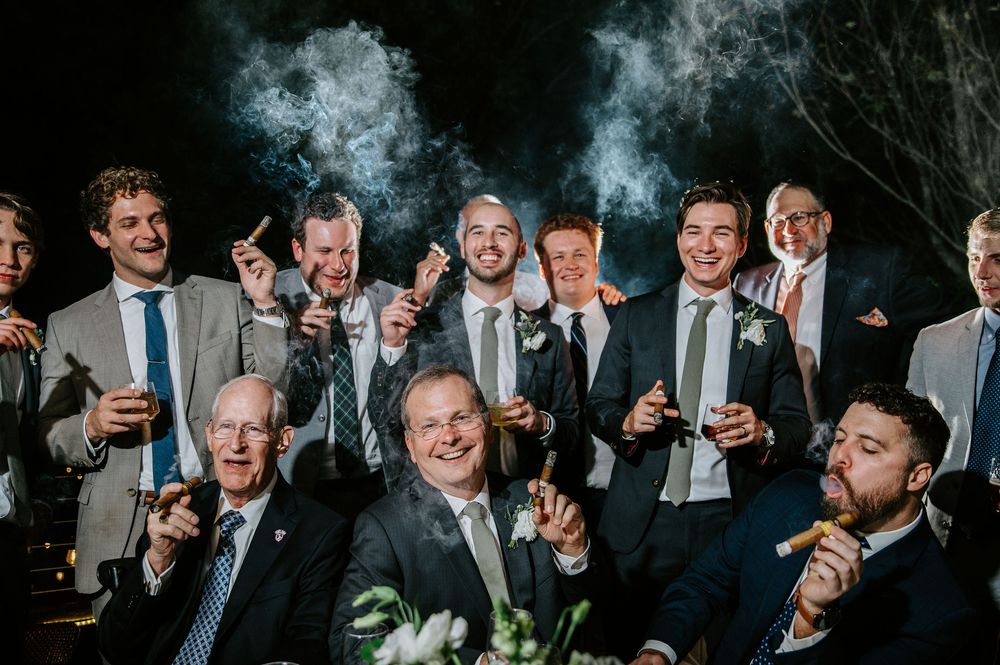 A group of formally dressed wedding guests raise their glasses in a celebratory toast during an evening reception.