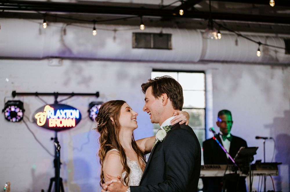 Wedding guests dance and celebrate at an indoor reception venue with decorative lighting and rustic decor.