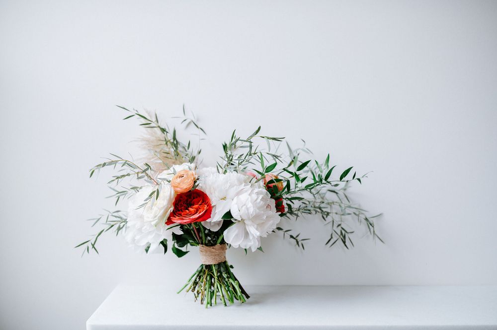 A delicate white and red floral bouquet with greenery arranged on a light gray background.