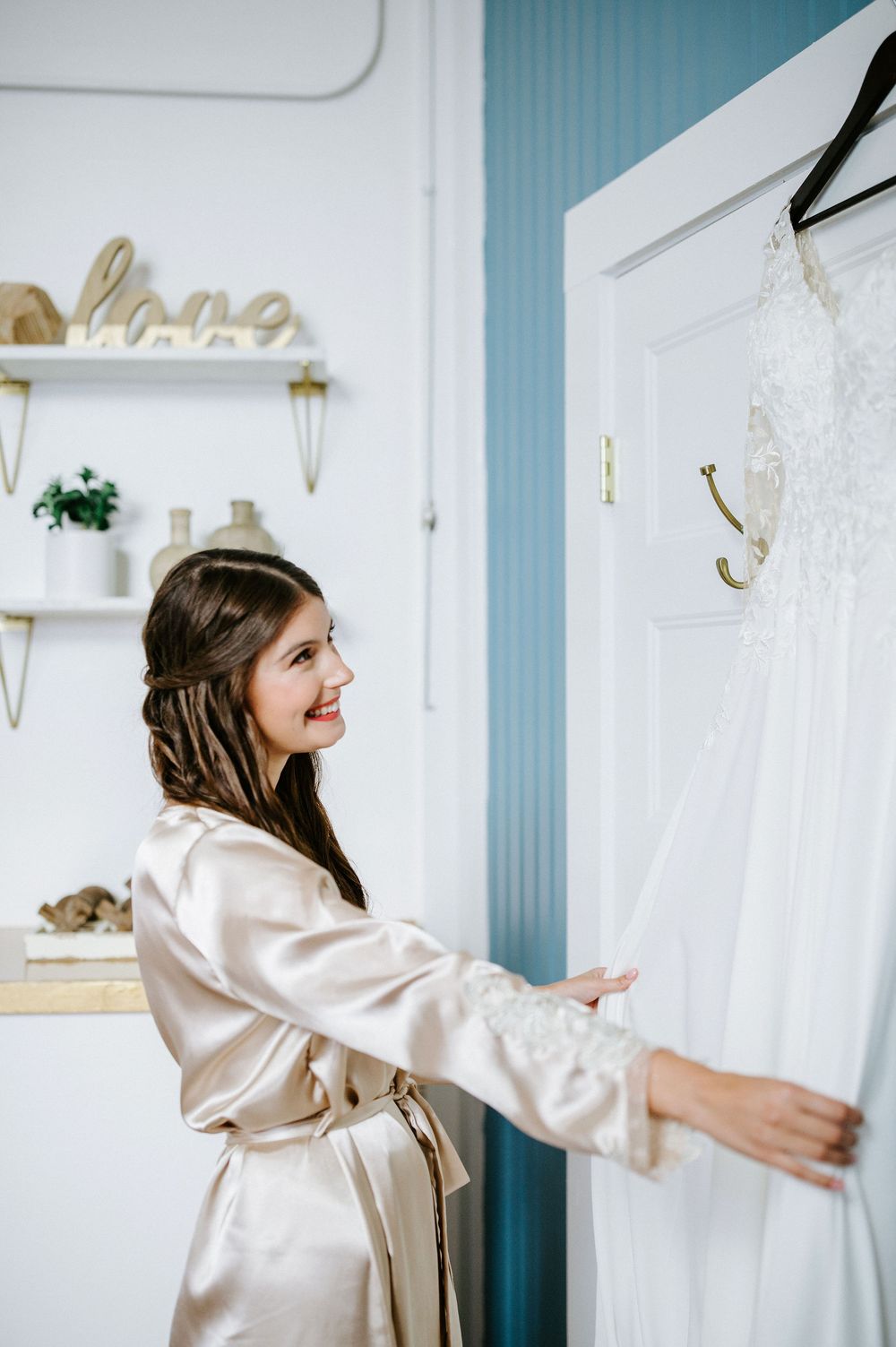 A person wearing a silky champagne-colored robe reaches for something while standing in a room with blue striped walls.