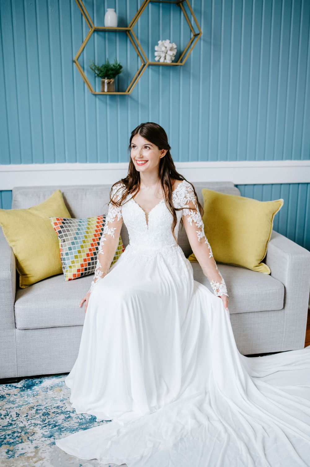 White wedding dress displayed against light blue walls and yellow accent pillows on gray sofa.