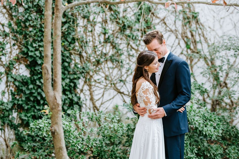 Romantic outdoor wedding photo series showing couple embracing among trees and greenery in a garden setting.