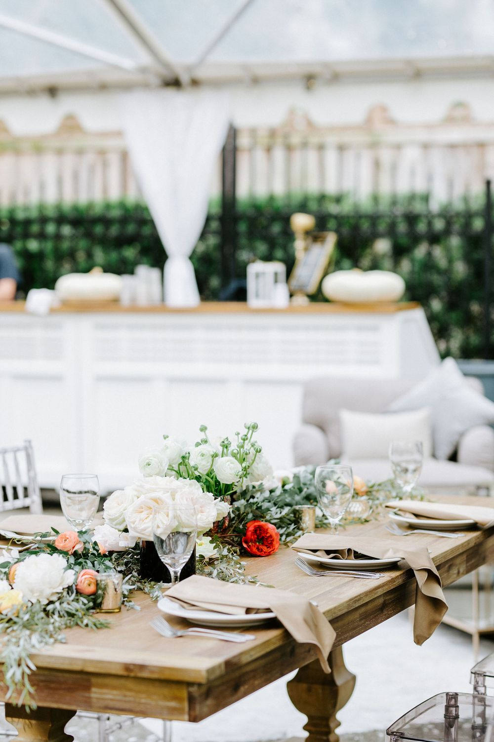 Elegant rustic wedding table setting with floral centerpieces and white linens under an outdoor tent canopy.