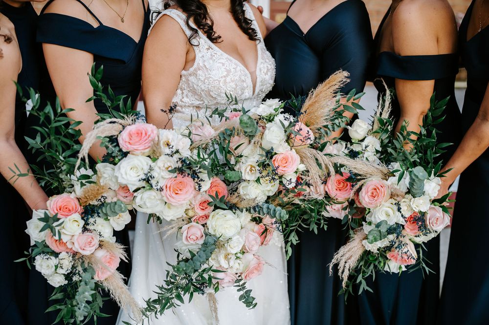 Wedding party members hold pink and white floral bouquets while wearing black dresses and a white bridal gown.