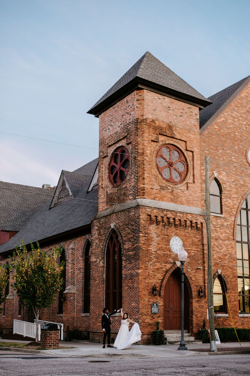 Exterior view of a traditional brick church building with arched windows and round clock tower.