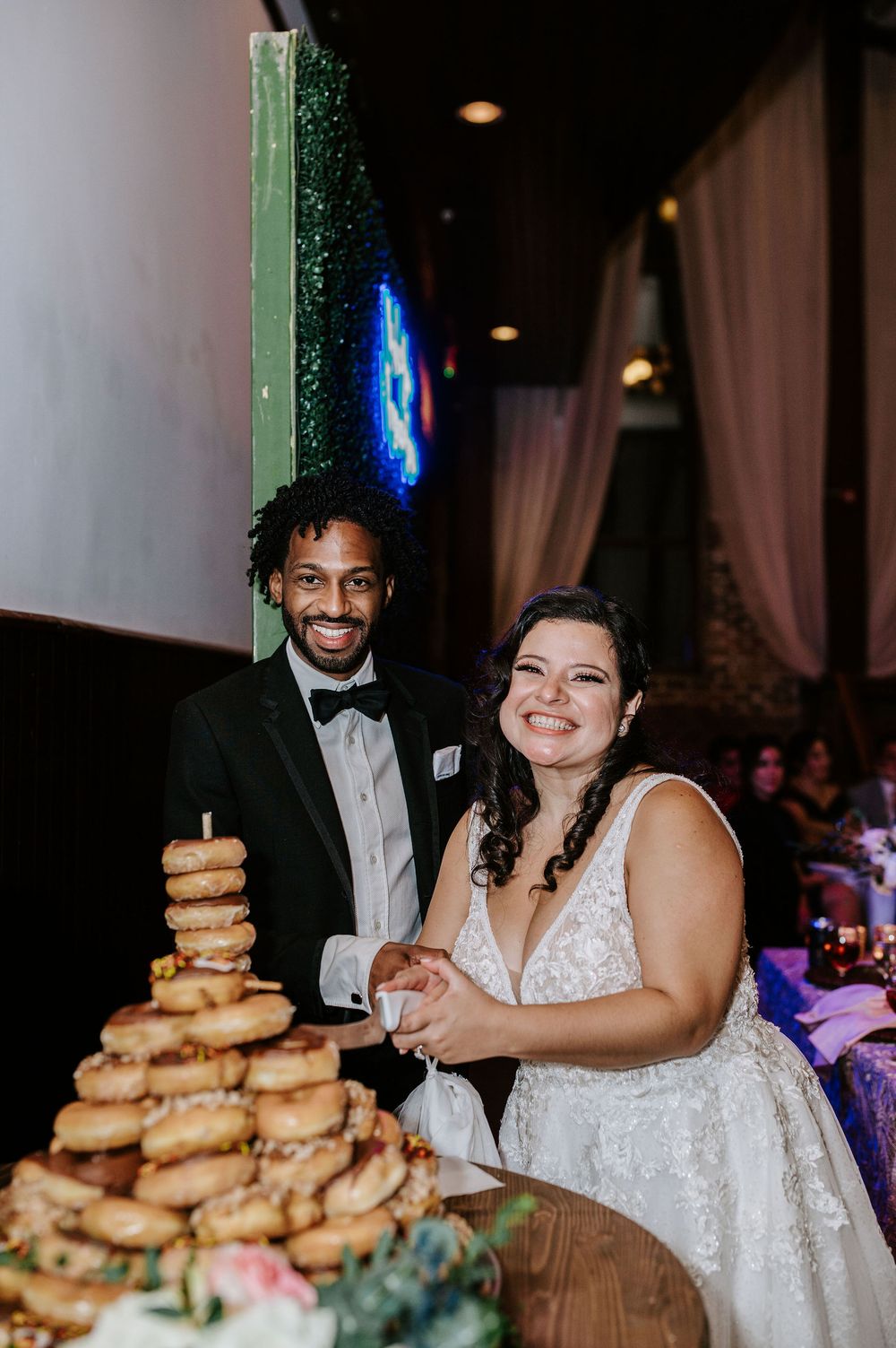 Newlyweds share a joyful moment at their reception table with a tower of donuts displayed nearby.