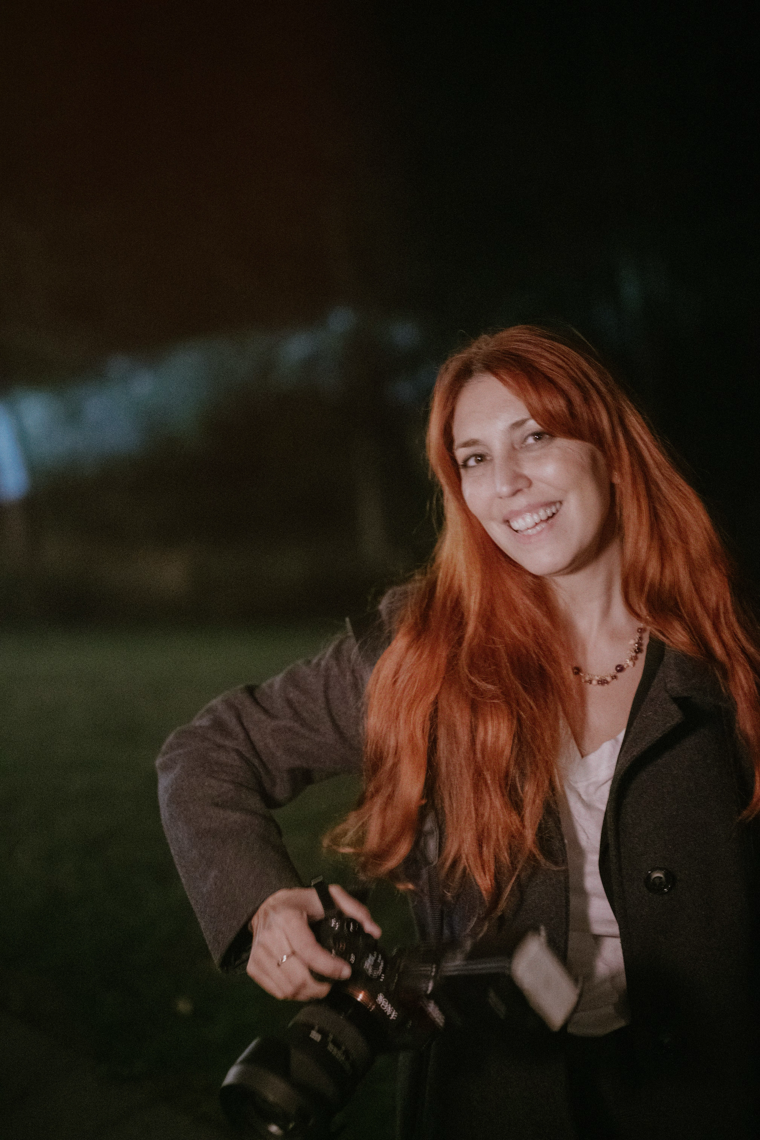A photographer with red hair captures photos at night with string lights in the background.