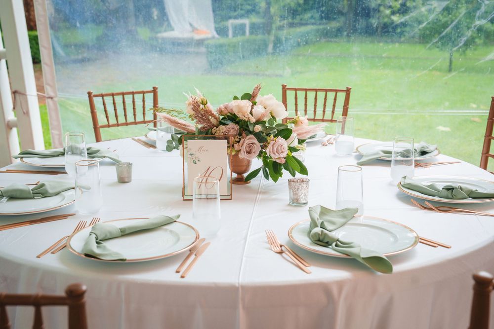 Elegant wedding reception table settings with white linens, floral centerpieces and chiavari chairs in a bright venue.