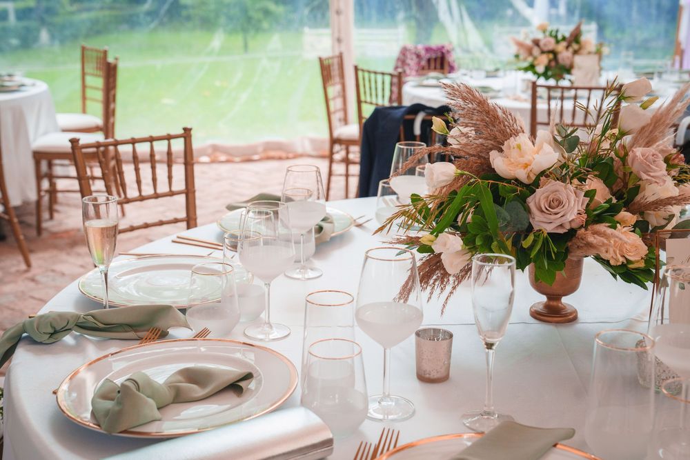 Elegant wedding reception tables decorated with pink floral centerpieces and crystal glassware in a light-filled venue.