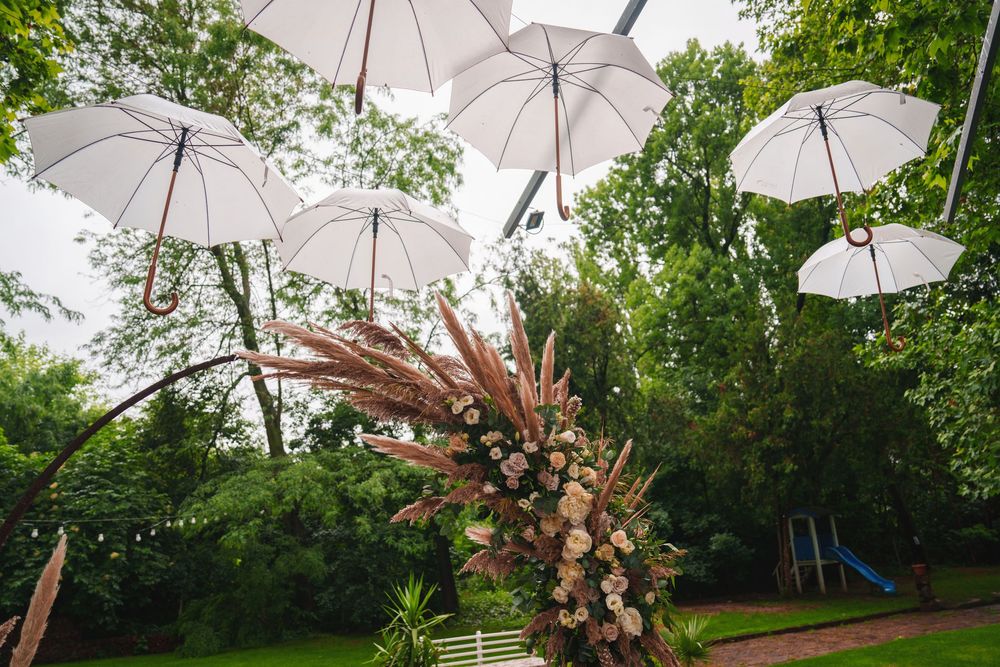 White umbrellas suspended over outdoor wedding space with boho-style dried floral installation and natural surroundings.
