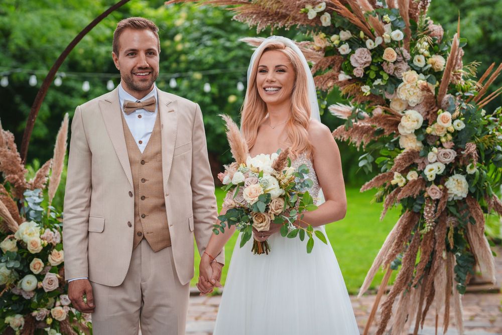 Newlyweds walk together on garden path with romantic floral decor and natural lighting.