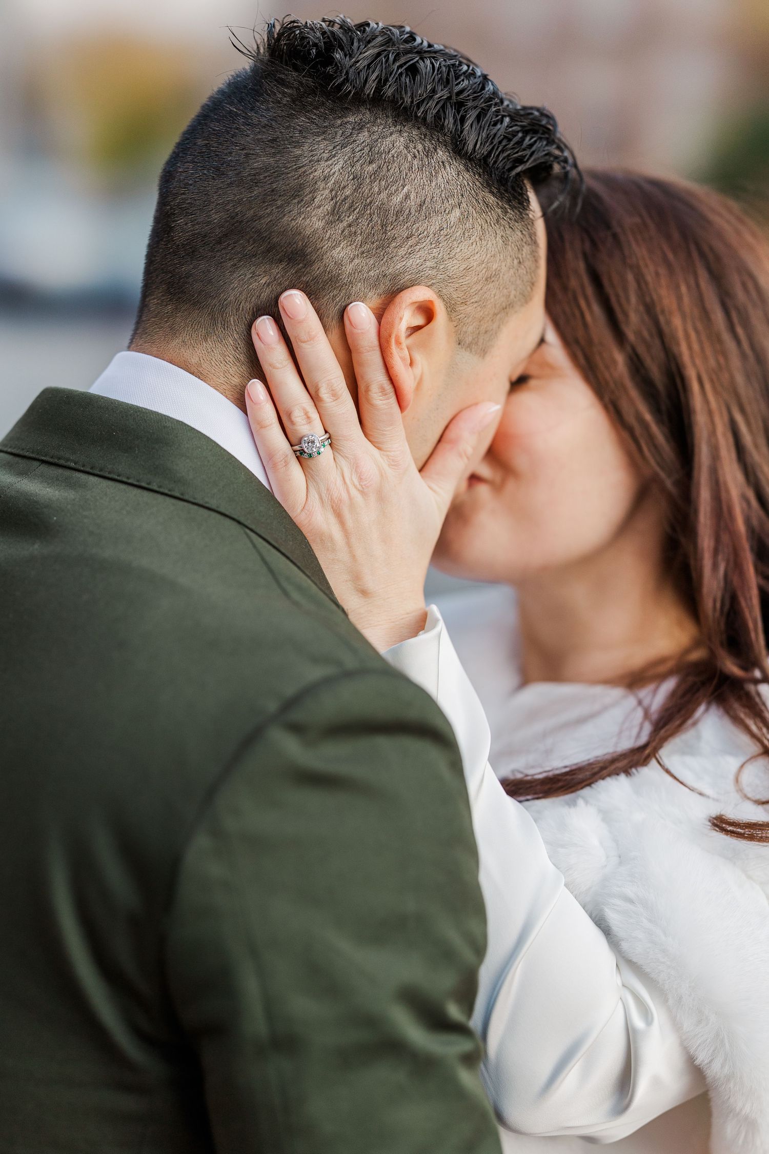 A romantic couple shares a tender kiss while the woman's hand shows off an engagement ring.