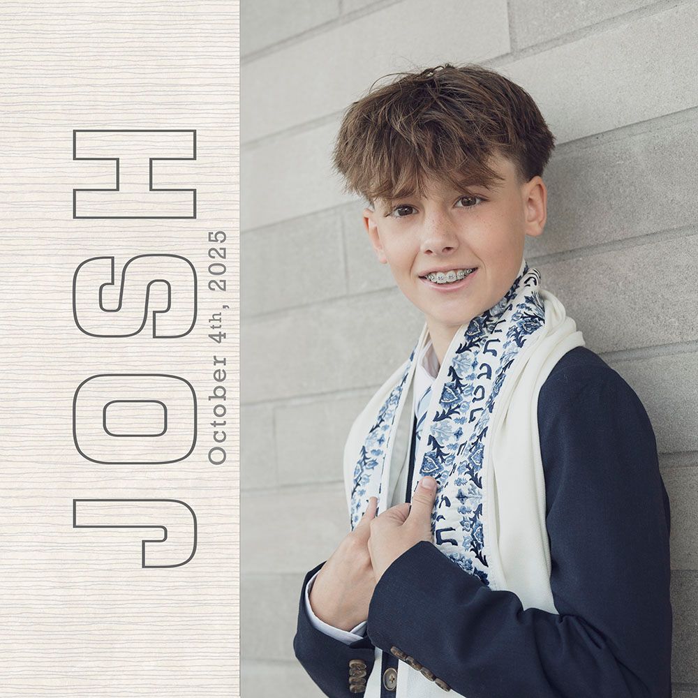 Person in navy suit jacket with blue and white patterned scarf smiling and posing against gray wall.