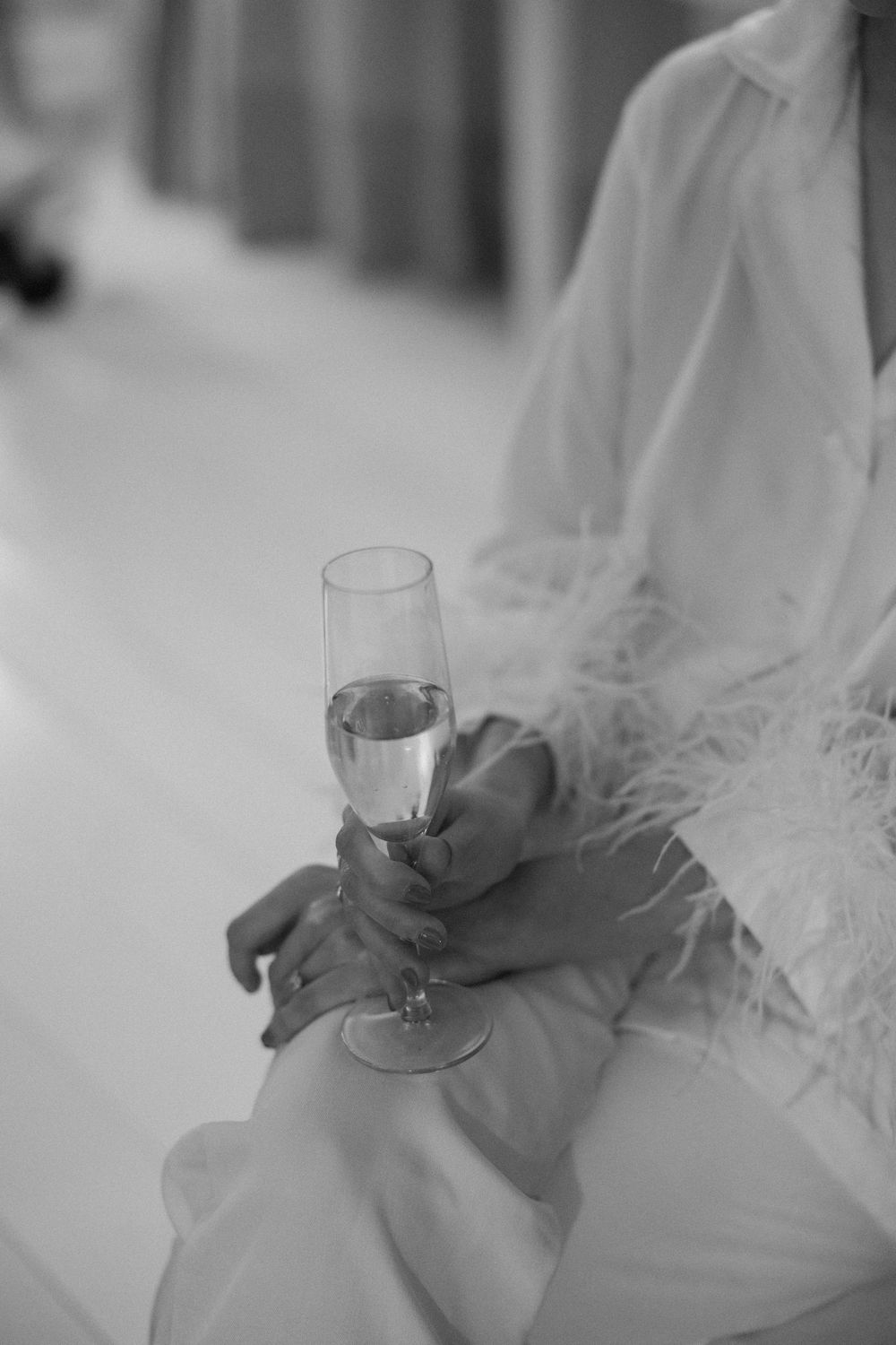 Close-up view of a bride's hands holding a champagne glass, showing details of her white lace dress.