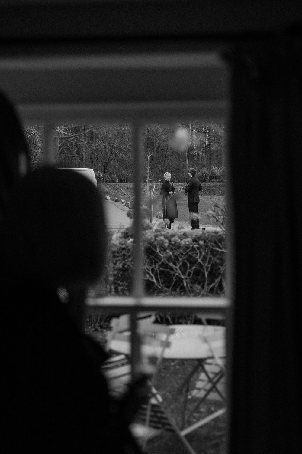 Silhouetted figures viewed through a window frame in black and white.