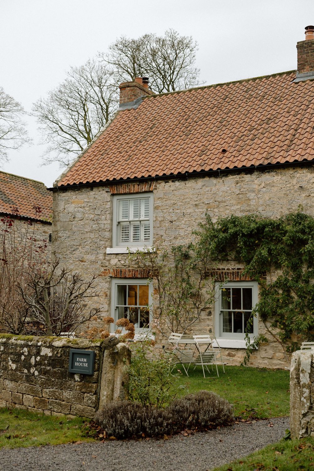 Rustic stone cottages with terracotta roofs and white windows in countryside setting.