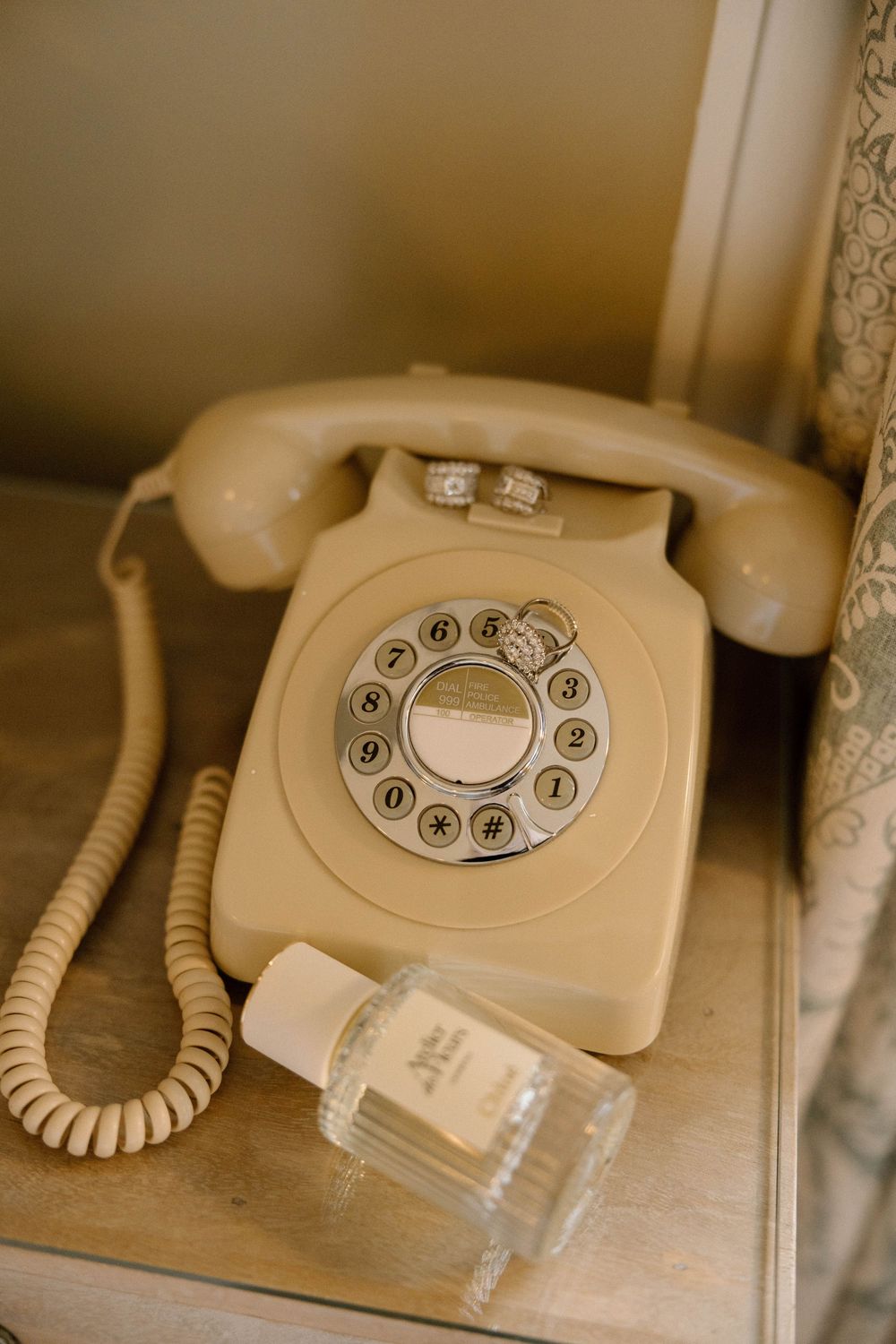 Vintage rotary telephone with wedding rings placed on top in a soft beige setting.