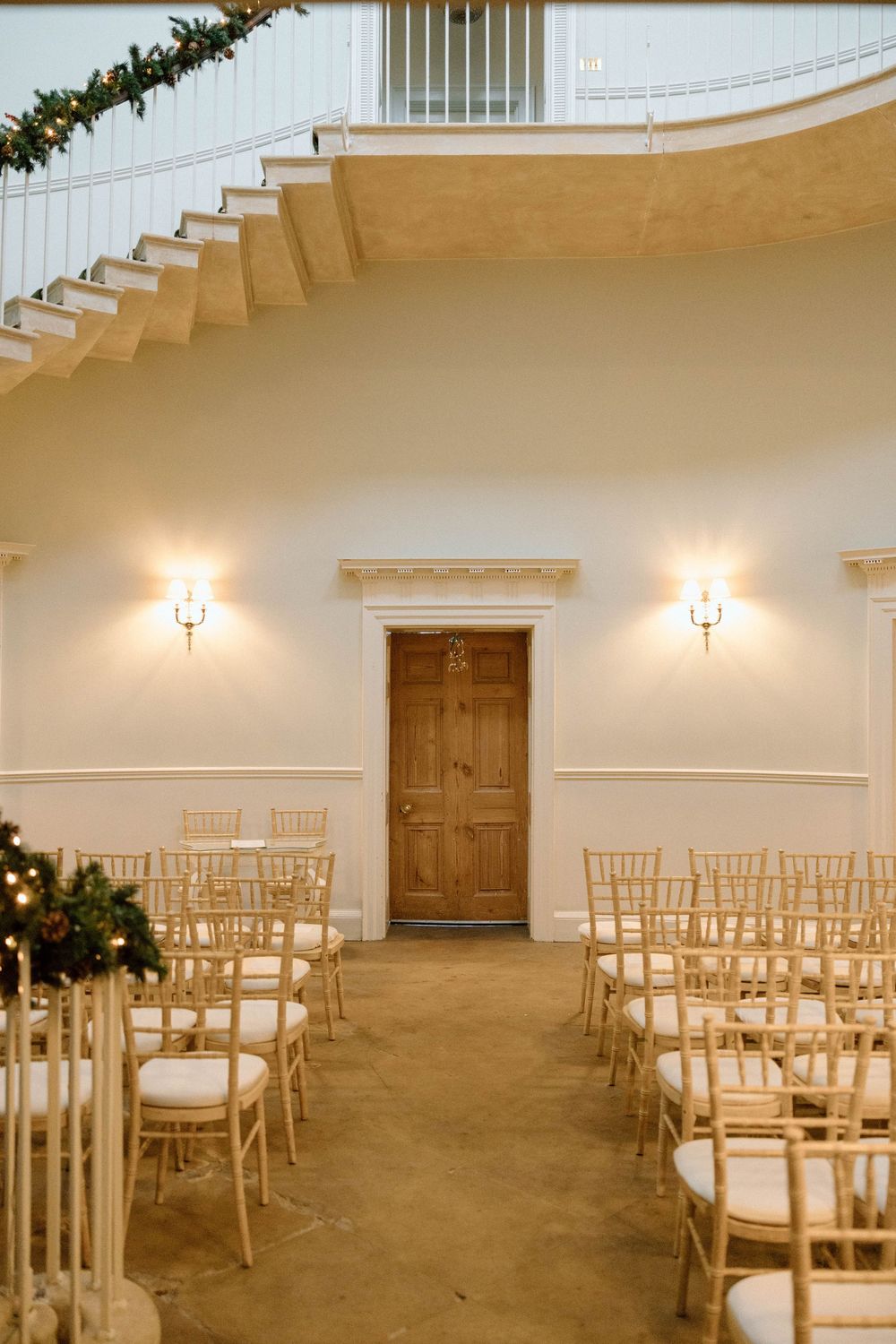 Wedding ceremony setup with white chairs and curved staircase in an elegant indoor venue.