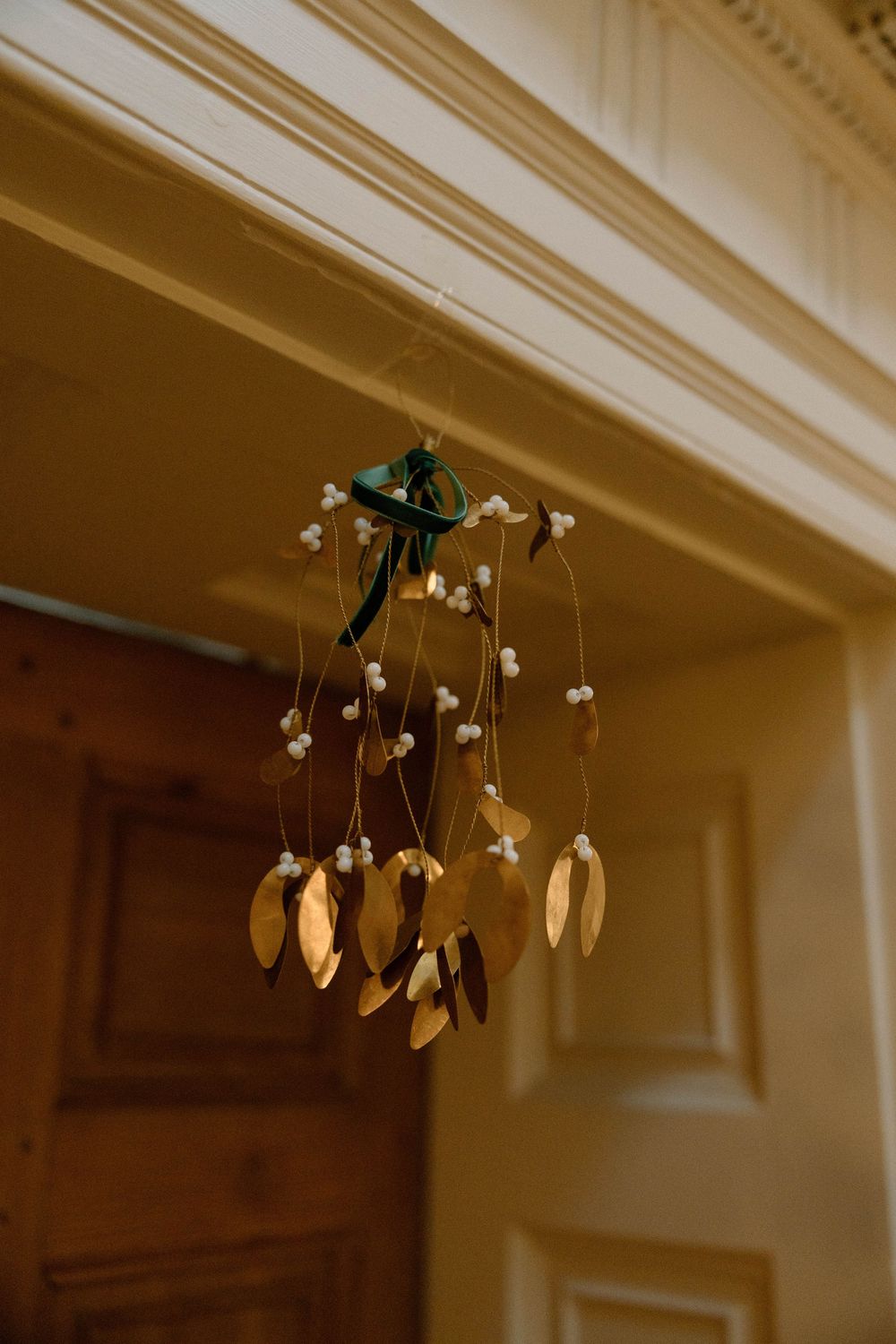 A delicate hanging decoration with white flowers and golden leaves suspended from an ornate ceiling.