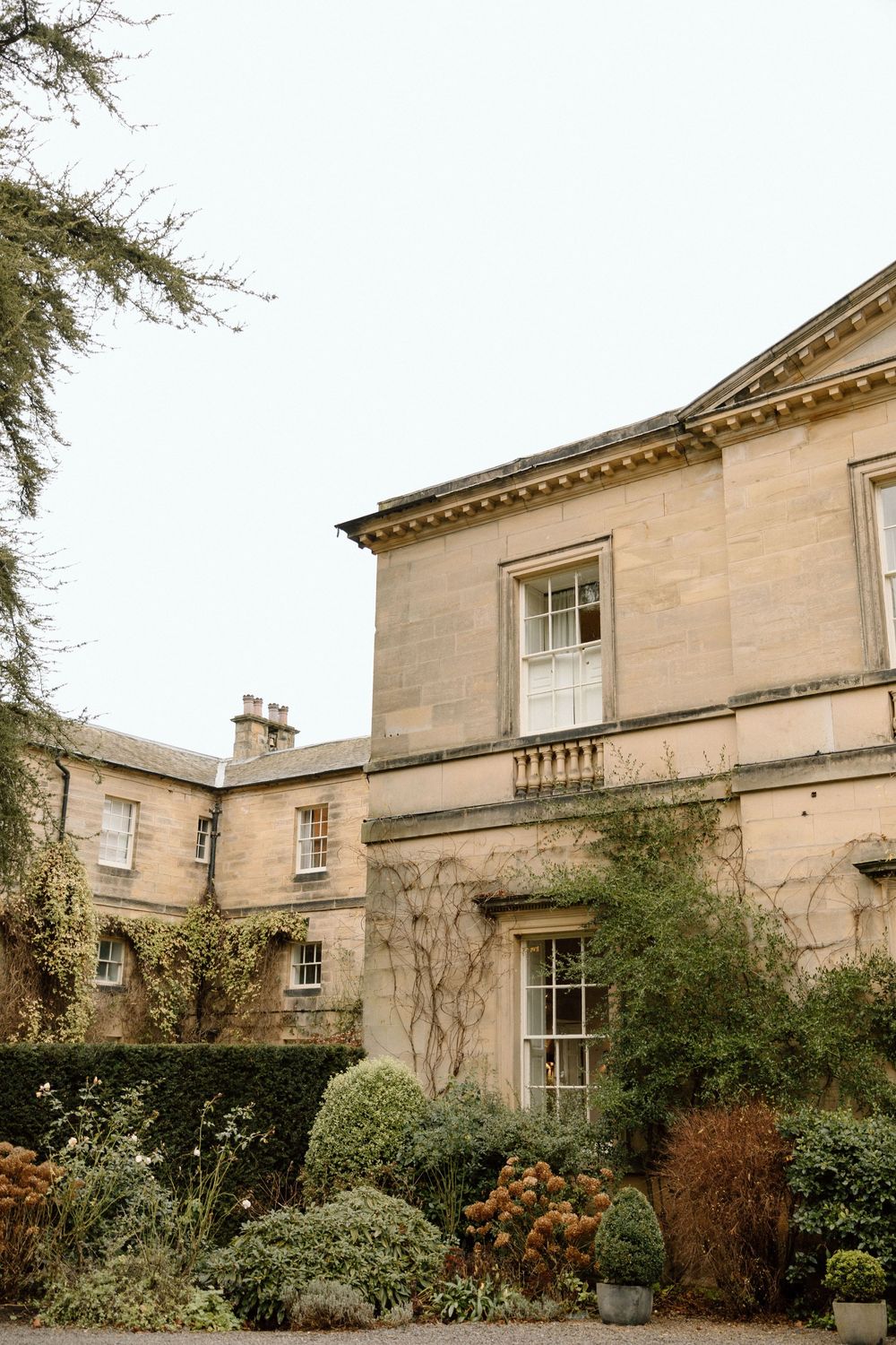 Exterior view of a grand stone mansion with Georgian architecture and manicured gardens.