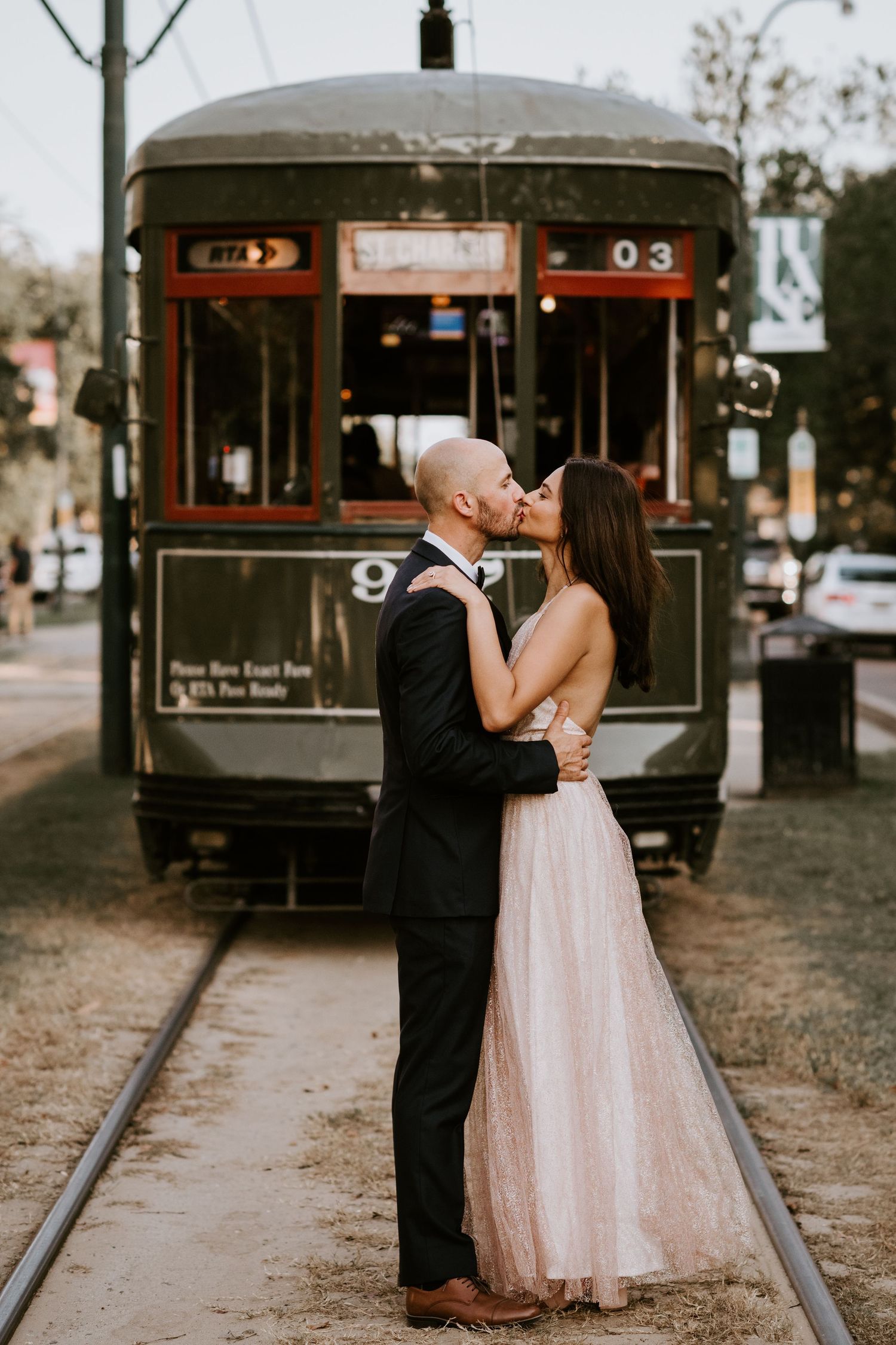 Bride and groom share a romantic kiss in front of a vintage green streetcar in New Orleans.