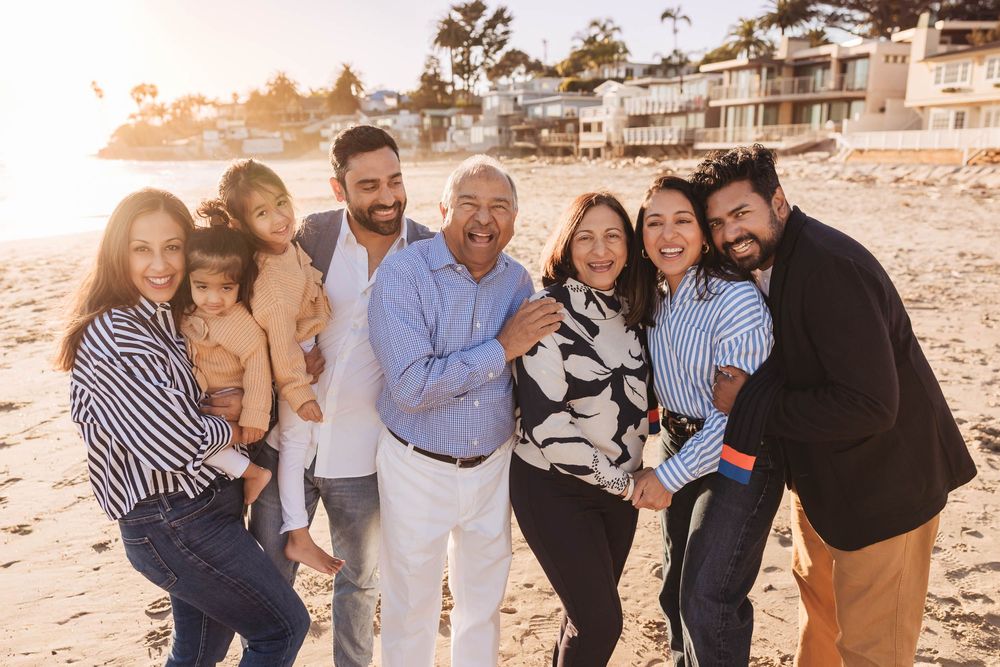 A group of people gather on a sandy beach at sunset wearing casual attire and embracing each other.