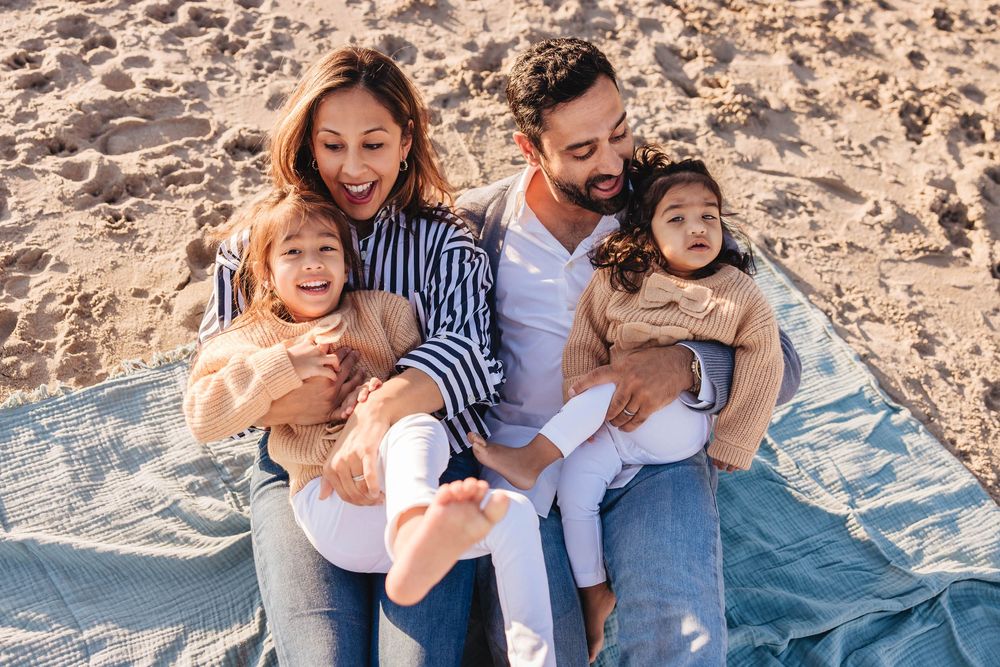 A family enjoys a playful moment together on a rocky beach with blue water in the background.