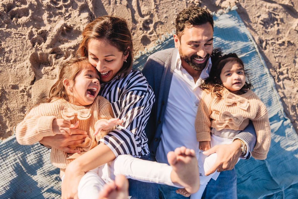 Family laughing together while sitting on a blanket at the beach during a sunny day.