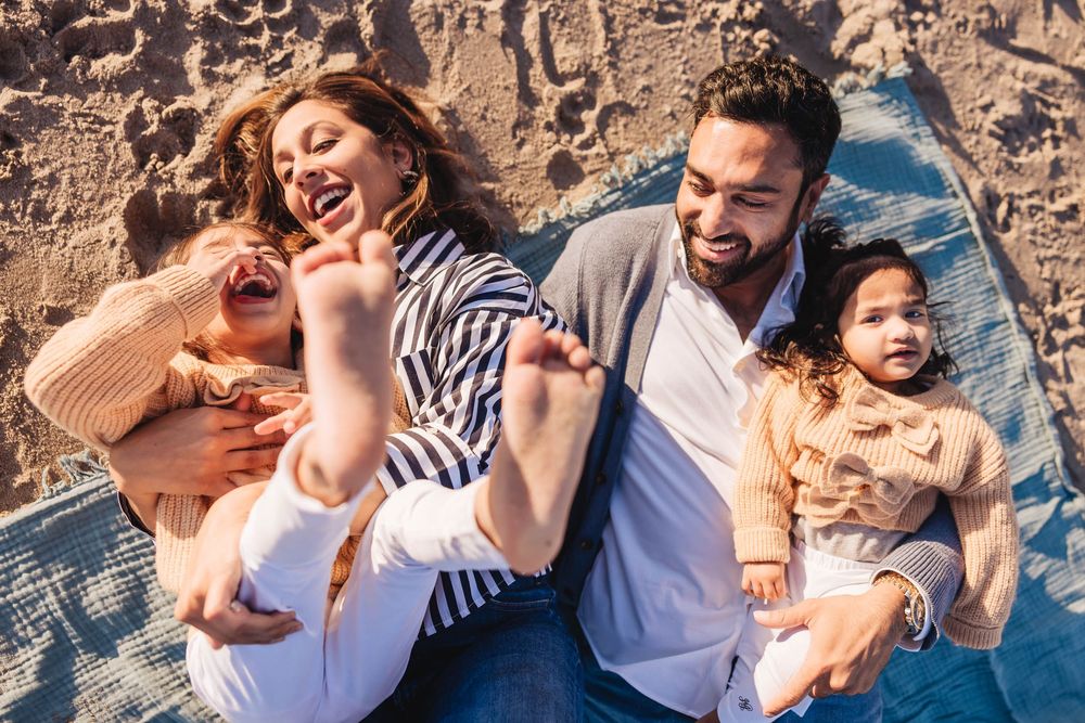 Happy family relaxing together on a blue blanket against a stone wall on a sunny day.