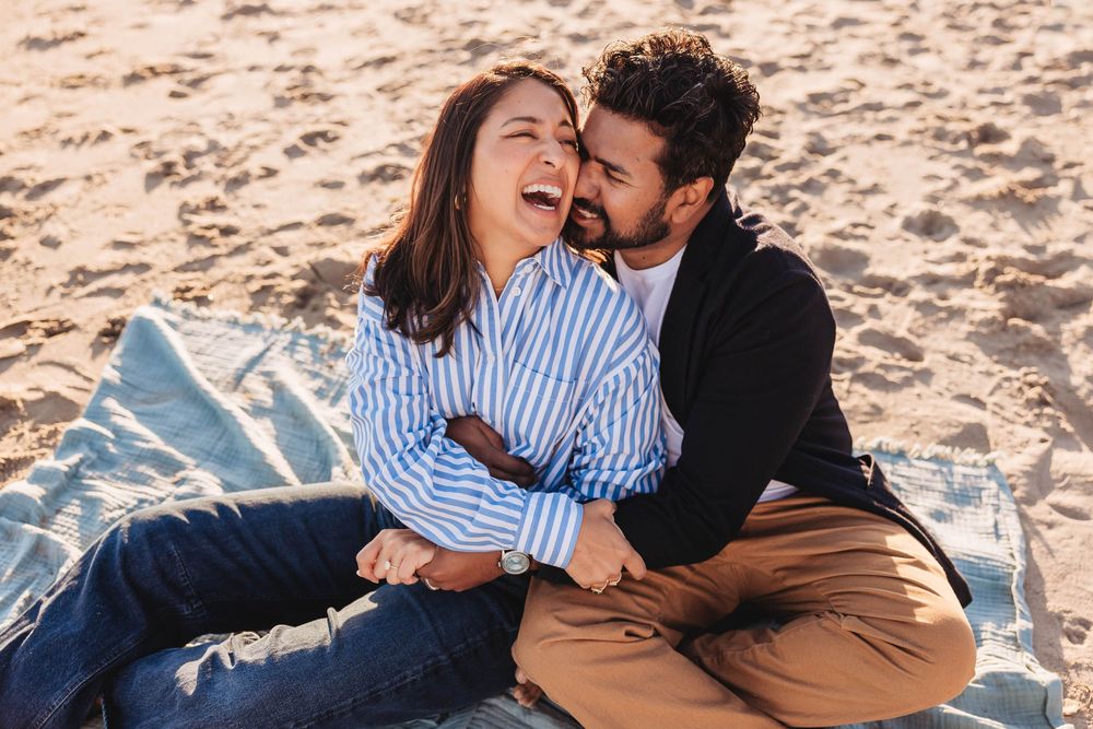 A couple shares tender moments while sitting together on a sandy beach at sunset.