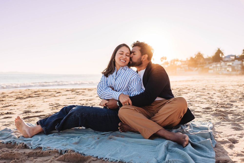 Couple relaxing together on a blanket at the beach during golden hour sunset.