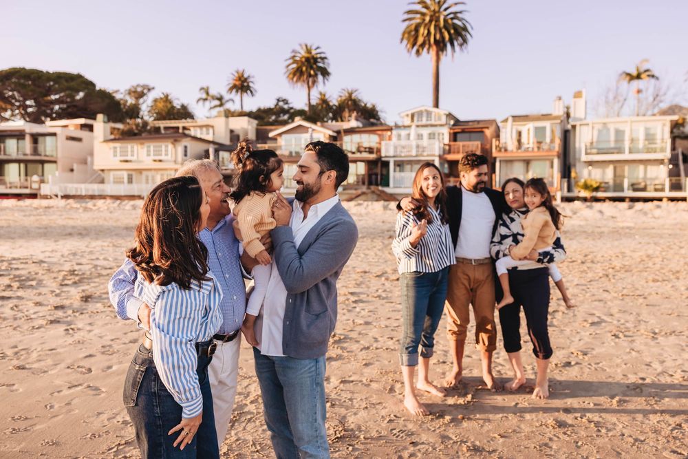 Group of people dancing together on a sandy beach at sunset with palm trees in the background.