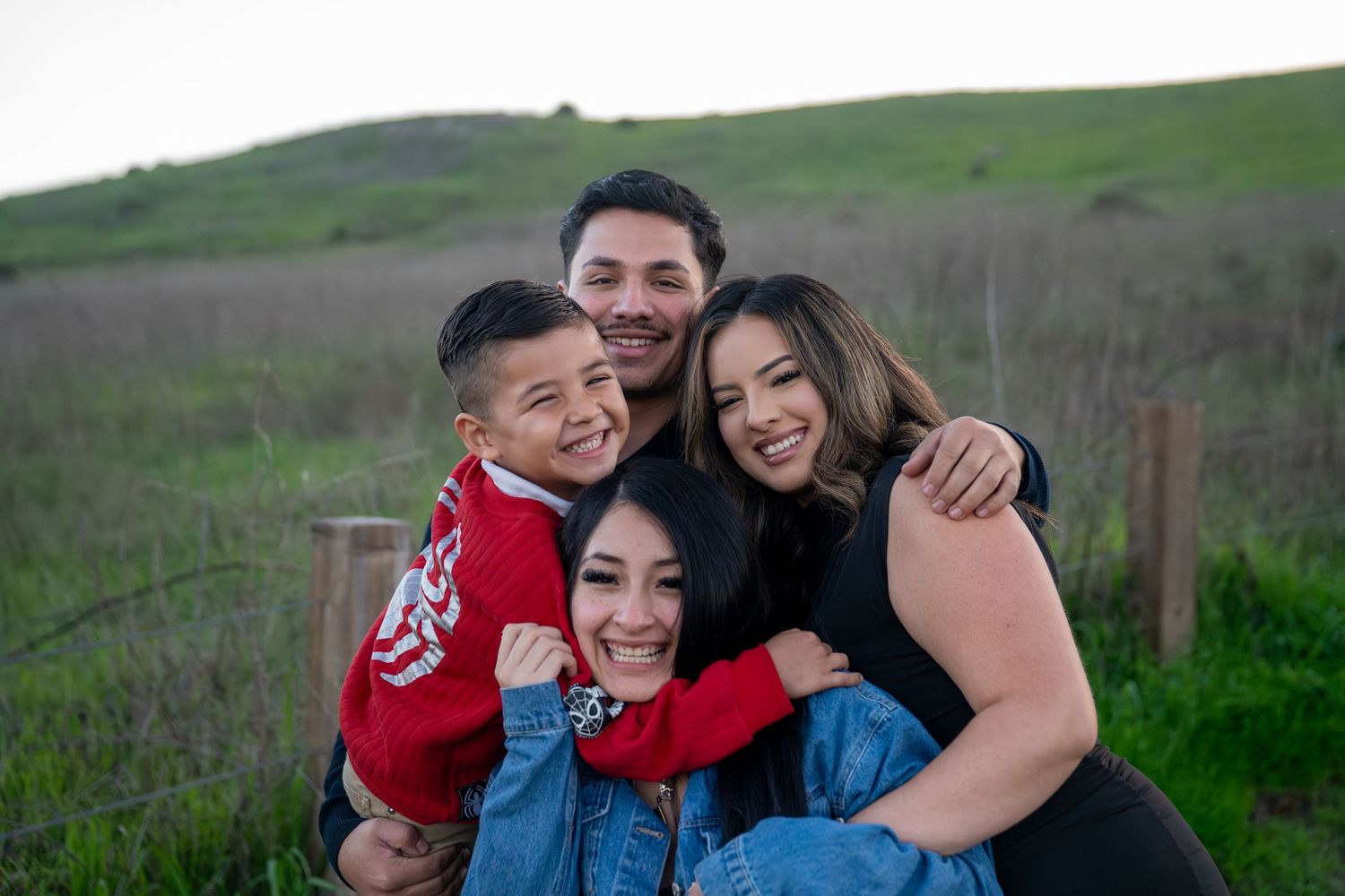 A happy group poses together outdoors on a green hillside during golden hour.