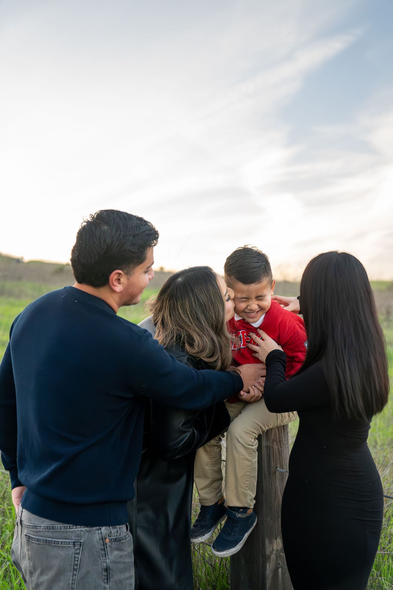 A family shares playful moments together while posing outdoors in a grassy field at sunset.