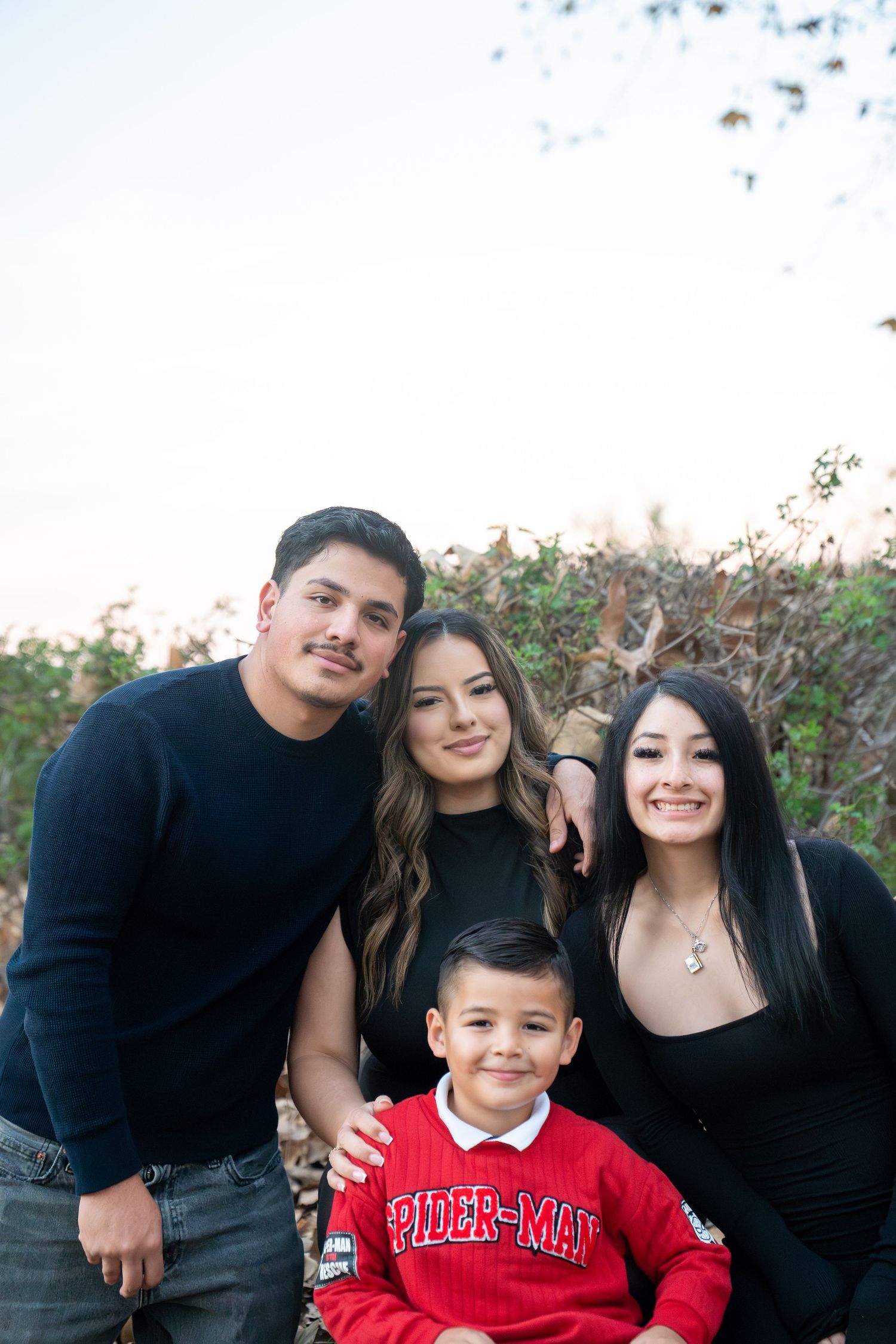 A family wearing black and red clothing poses together outdoors during a photo session.