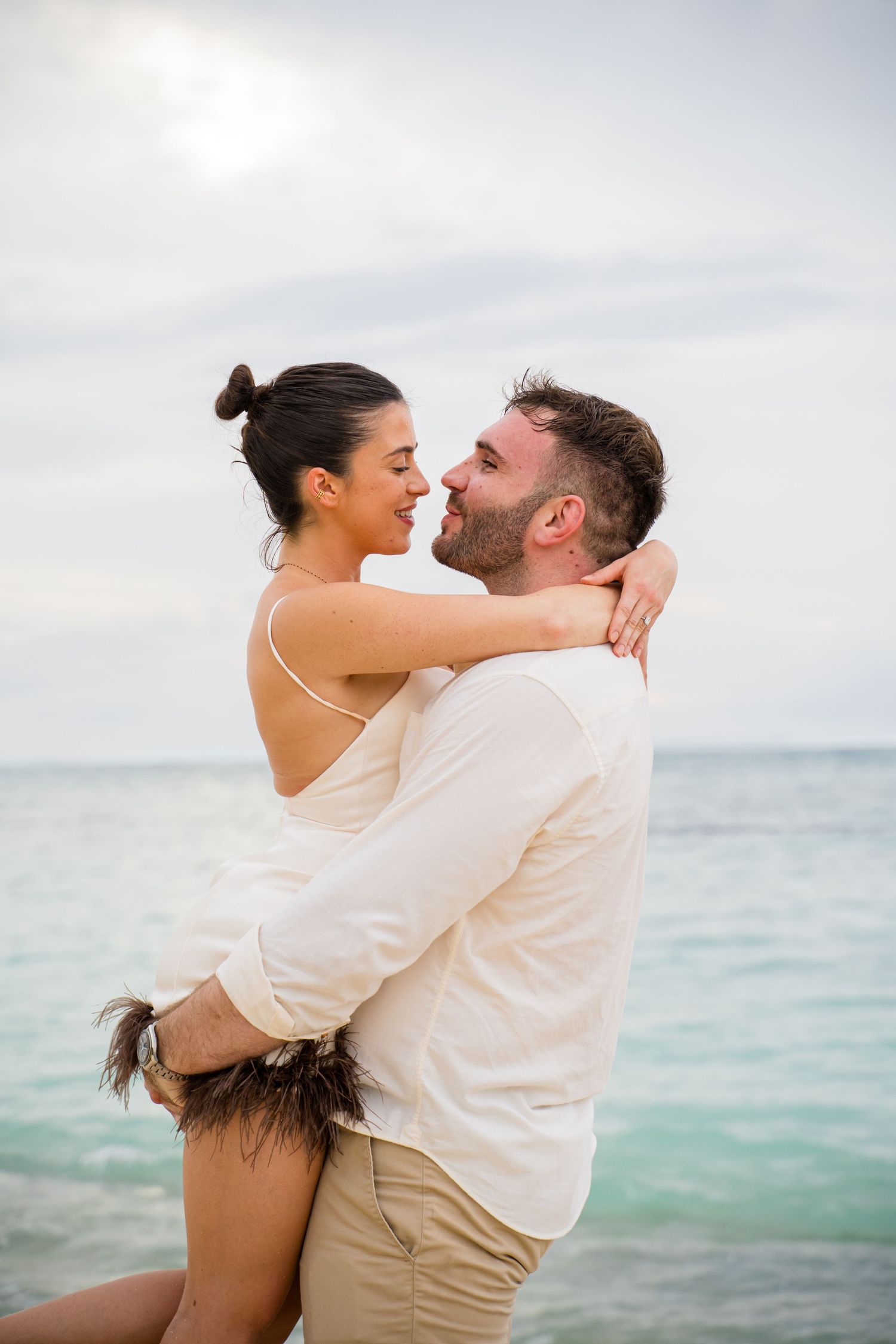 A couple shares an intimate moment on a beach with turquoise waters.