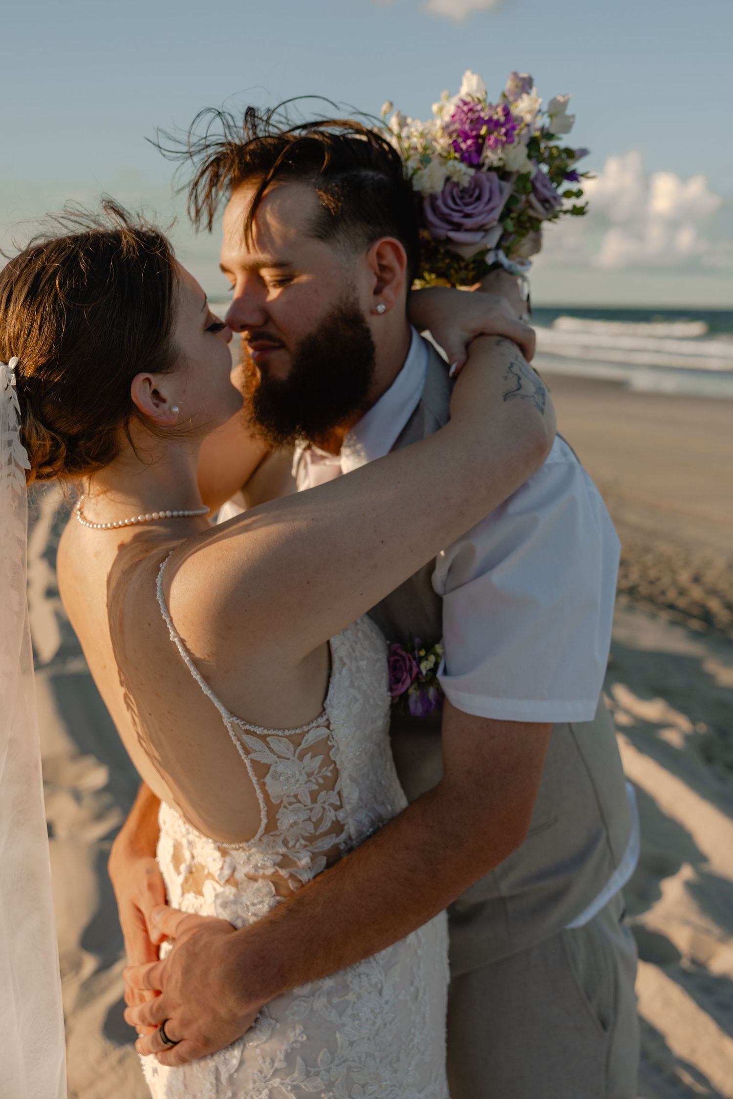Lace wedding dress with train hanging on wooden hanger in front of balcony window overlooking coastal beach houses.