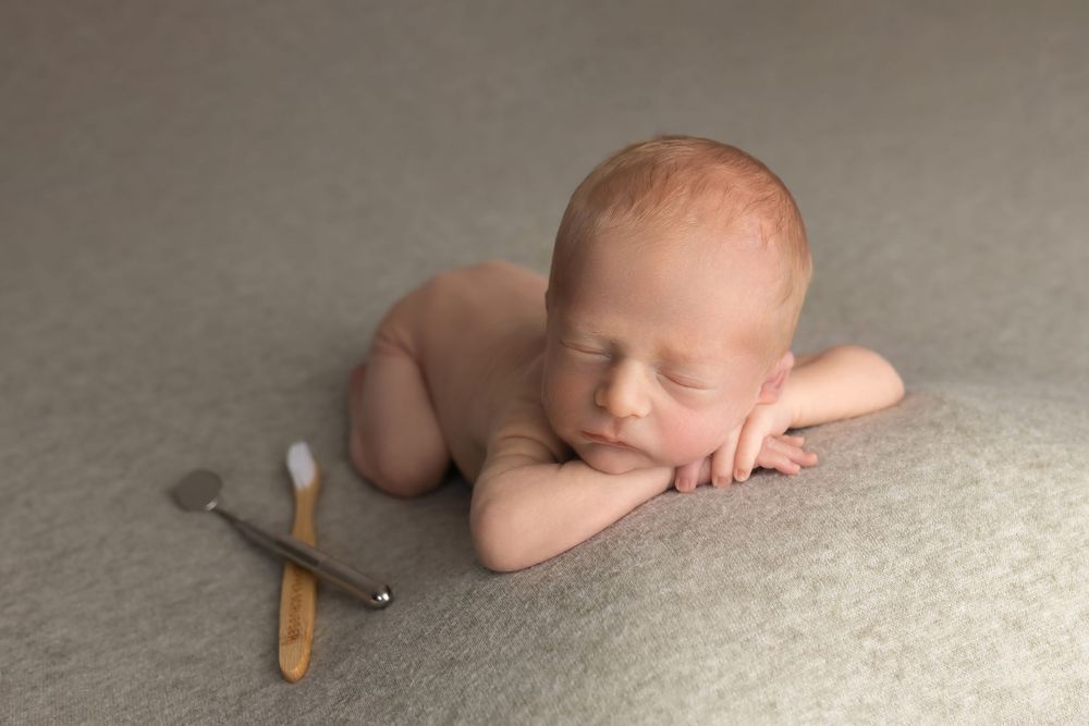 Newborn baby on green background with dental tools, taken by Jen Knightstep, Photographer